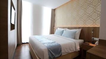 A hotel room with a large bed, a nightstand, a desk, and a patterned wall.