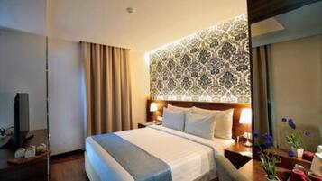 A hotel room with a large bed, a headboard with a patterned design, a bedside table with a lamp, and a nightstand with a vase of flowers.