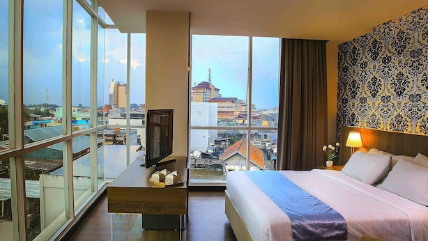 Une chambre d’hôtel avec une grande fenêtre, un lit, un bureau et un téléviseur.