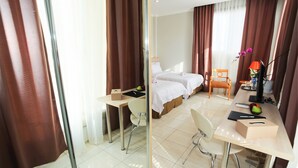 A hotel room with two beds, a desk, a chair, a small table, and a mirror. - Topaz Residence (Jakarta)