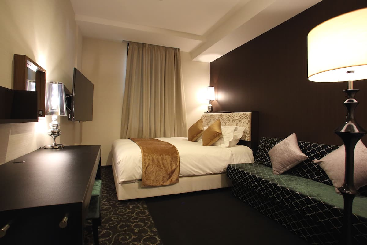 A hotel room with a bed, bedside table, lamp, and a TV.