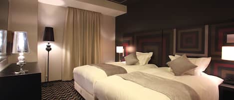 A hotel room with two beds, a desk, a lamp, and a patterned carpet.