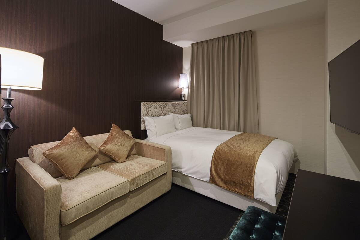 A hotel room with a bed, a sofa, a lamp, and a curtain.