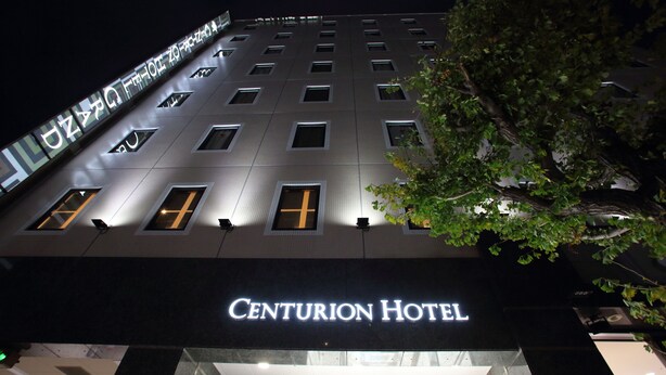 The exterior of the Centurion Hotel at night, featuring a modern facade with illuminated signage and a tree in the foreground. - Centurion Hotel Grand Kobe Station (Kobe)