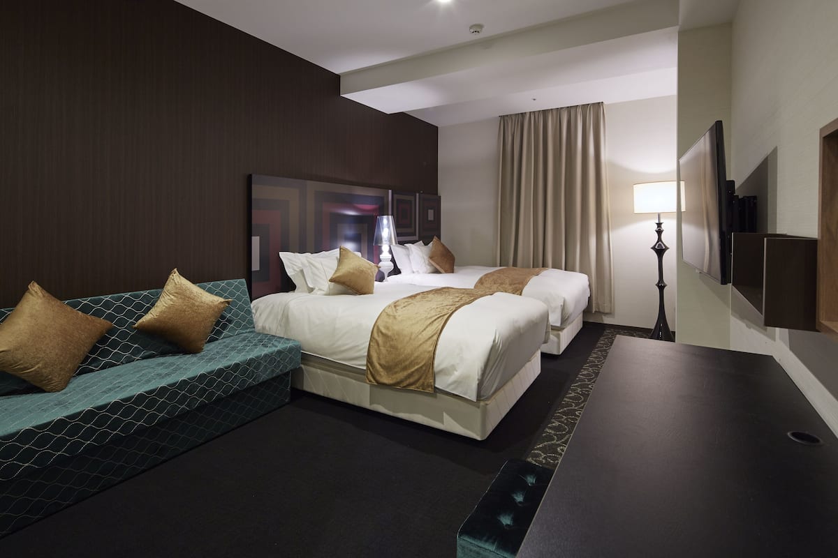 A hotel room with two beds, a sofa, a flat-screen TV, and a lamp.