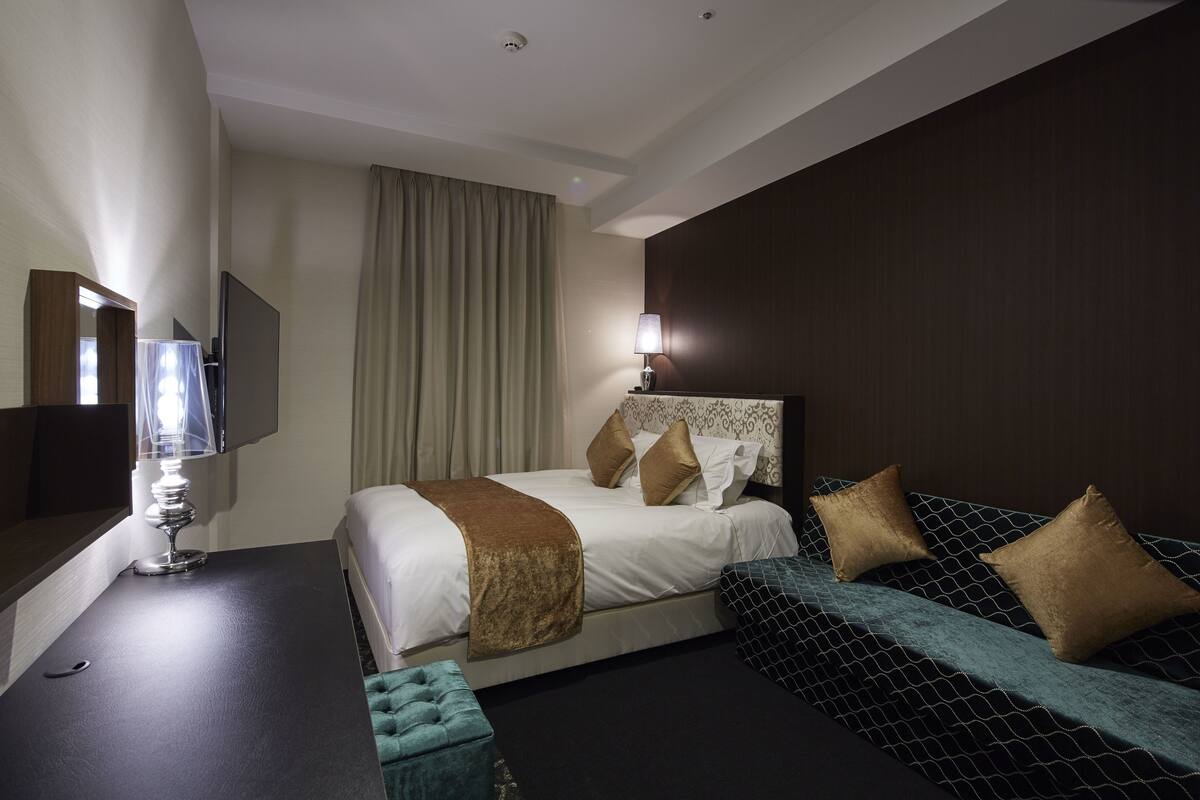 A hotel room with a bed, bedside table, lamp, and a TV.