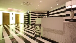 A hotel lobby with a modern design, featuring a marble reception desk, a glass partition, and a staircase with black and white stripes. - Centurion Hotel Grand Kobe Station (Kobe)