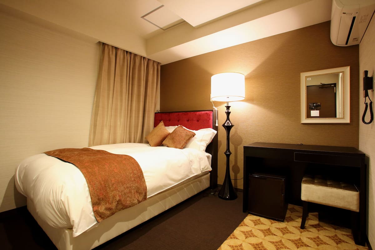 A hotel room with a bed, a desk, a lamp, a telephone, and a mirror.