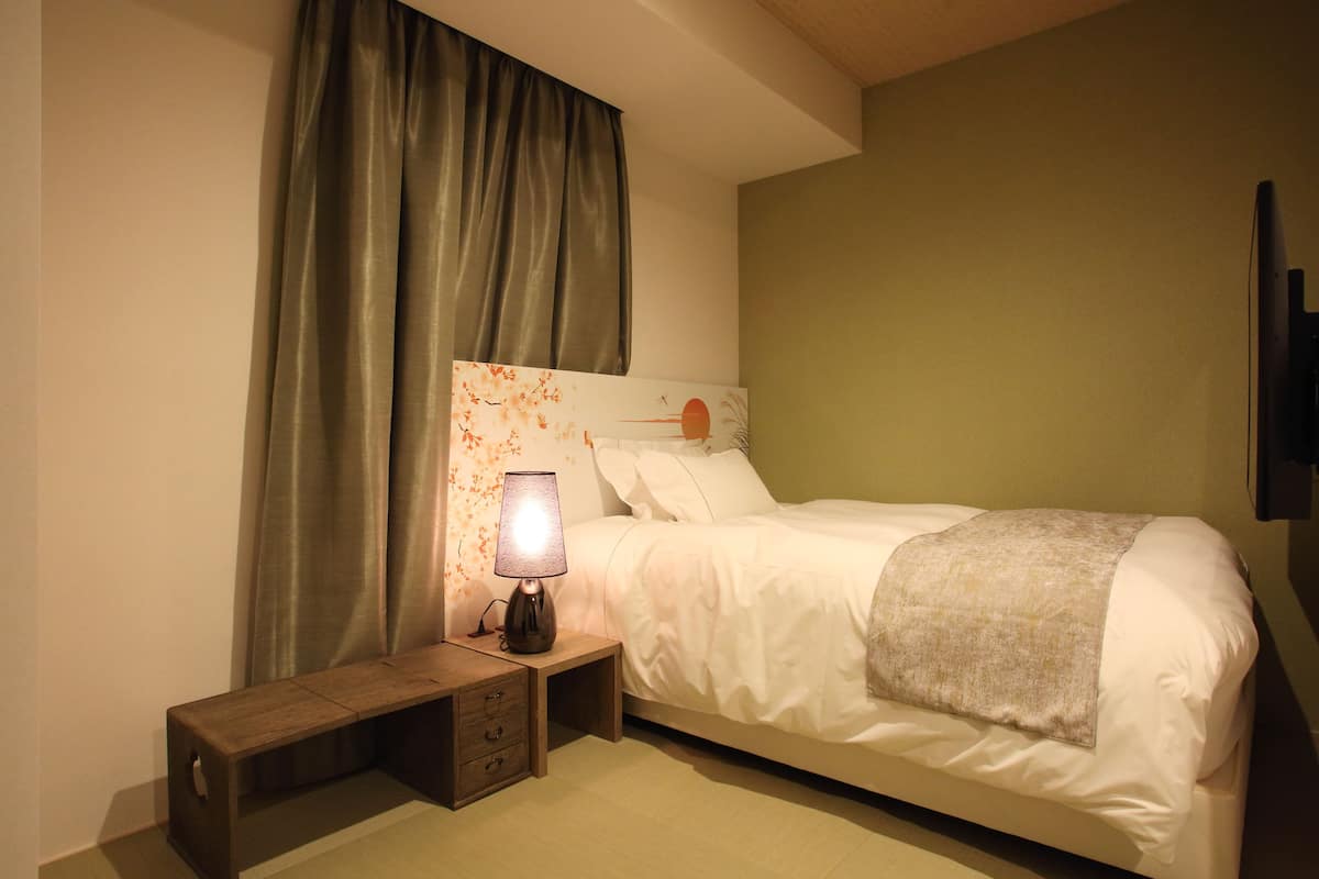 A neatly made bed with white linens, a bedside table with a lamp, and a wall-mounted TV.