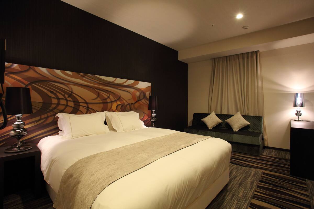 A hotel room with a large bed, a sofa, a desk, and a lamp.