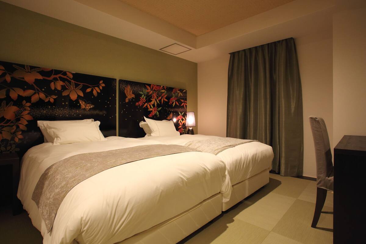 A hotel room with two beds, a large floral headboard, a desk, and a chair.