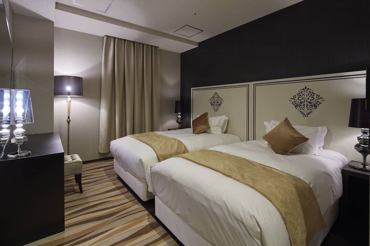A hotel room with two beds, a desk with a lamp, a large mirror, and a patterned carpet.