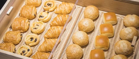 A wooden box containing various baked goods, including croissants and bread rolls.