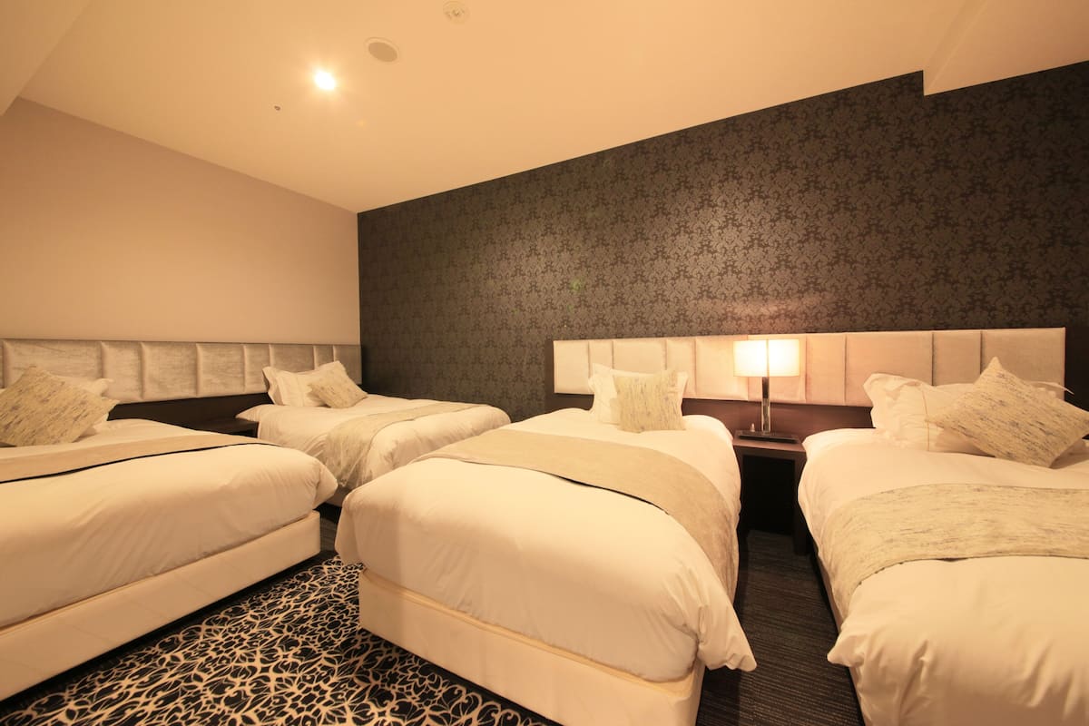 A hotel room with three beds, a patterned carpet, and a dark patterned wall.