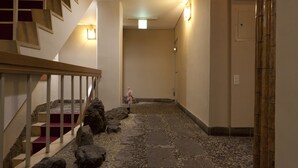 A hallway with a stone pathway, a wooden staircase with red steps, and a small pink statue. - Shin-Okubo Sekitei Hotel (Tokyo)