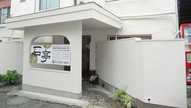 A white building with a sign for a business hotel, including a contact number and pricing information. - Shin-Okubo Sekitei Hotel (Tokyo)