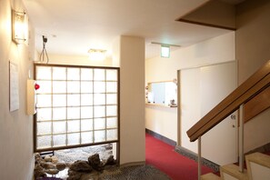 A hallway with a red carpet, a wooden staircase, and a large window with a grid pattern.