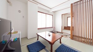 A traditional Japanese room with tatami flooring, a low wooden table, a desk with a computer, and a sliding door. - Shin-Okubo Sekitei Hotel (Tokyo)