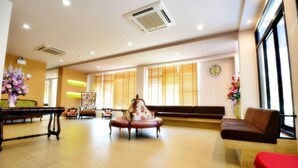 A spacious lobby with a wooden floor, a floral armchair, a sofa, and a red table. - Na Tubthieng Boutique Resort (Trang)