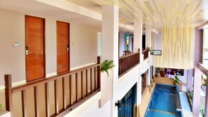 A hotel interior with a pool, wooden doors, and a balcony with a railing. - Na Tubthieng Boutique Resort (Trang)