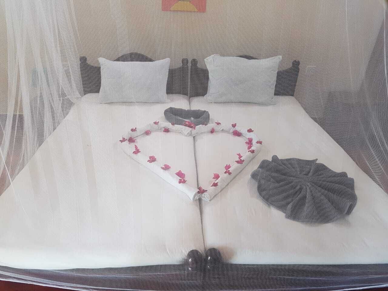 A bed with a heart-shaped decoration made of fabric and flowers, a gray fabric item on the bed, and a mosquito net over the bed.