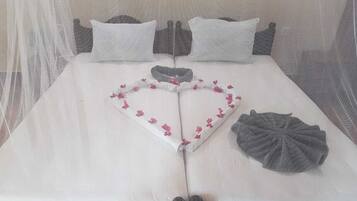 A bed with a heart-shaped decoration made of fabric and flowers, a gray fabric item on the bed, and a mosquito net over the bed.