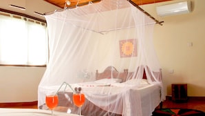A bedroom with a canopy bed, a bedside table with a drink, and a decorative rug. - Secret Escape Nilaveli Ayurveda Hotel & Spa (Nilaveli)