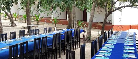 An outdoor dining area with long tables covered in blue tablecloths, surrounded by wooden chairs.
