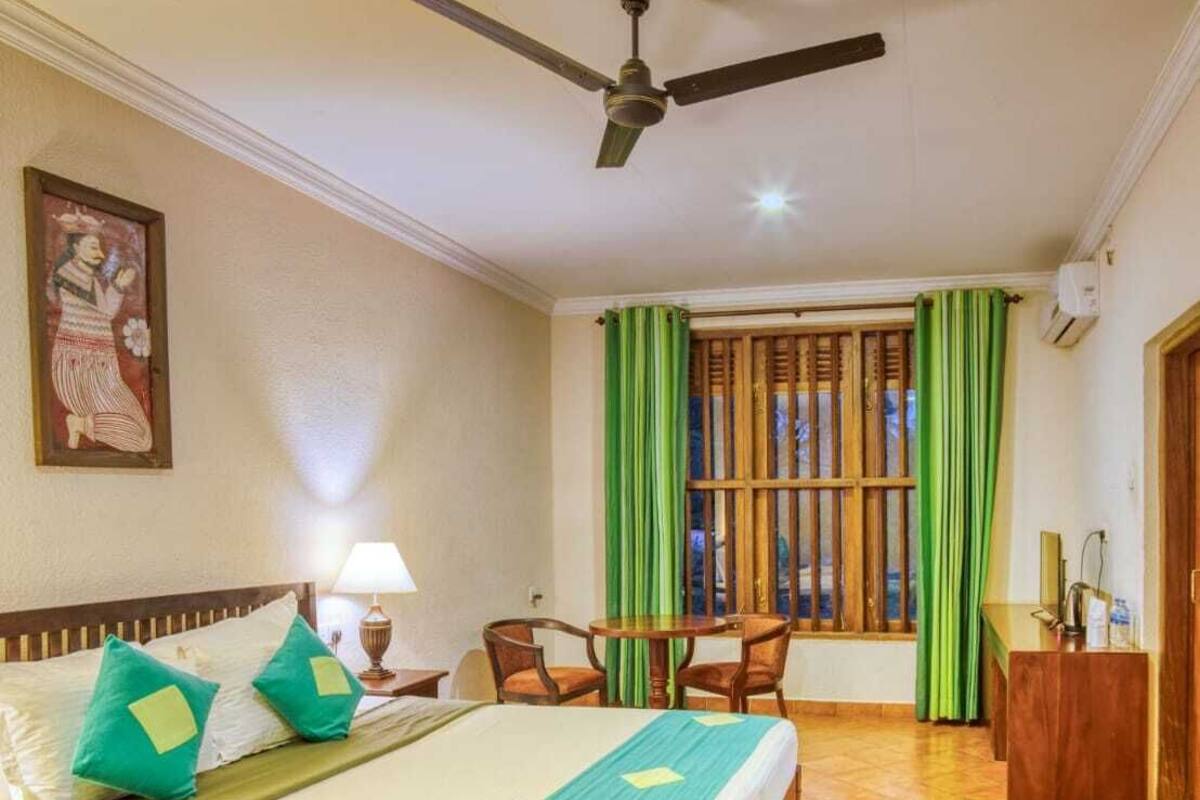 A hotel room with a bed, a desk, a chair, a ceiling fan, and a window with curtains.
