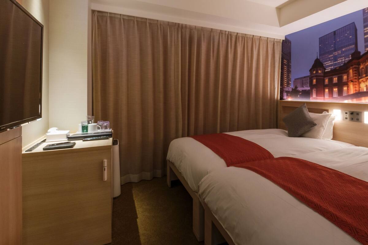 Ein Hotelzimmer mit Bett, Schreibtisch, Telefon, Tasse sowie Blick auf die Stadtlandschaft.