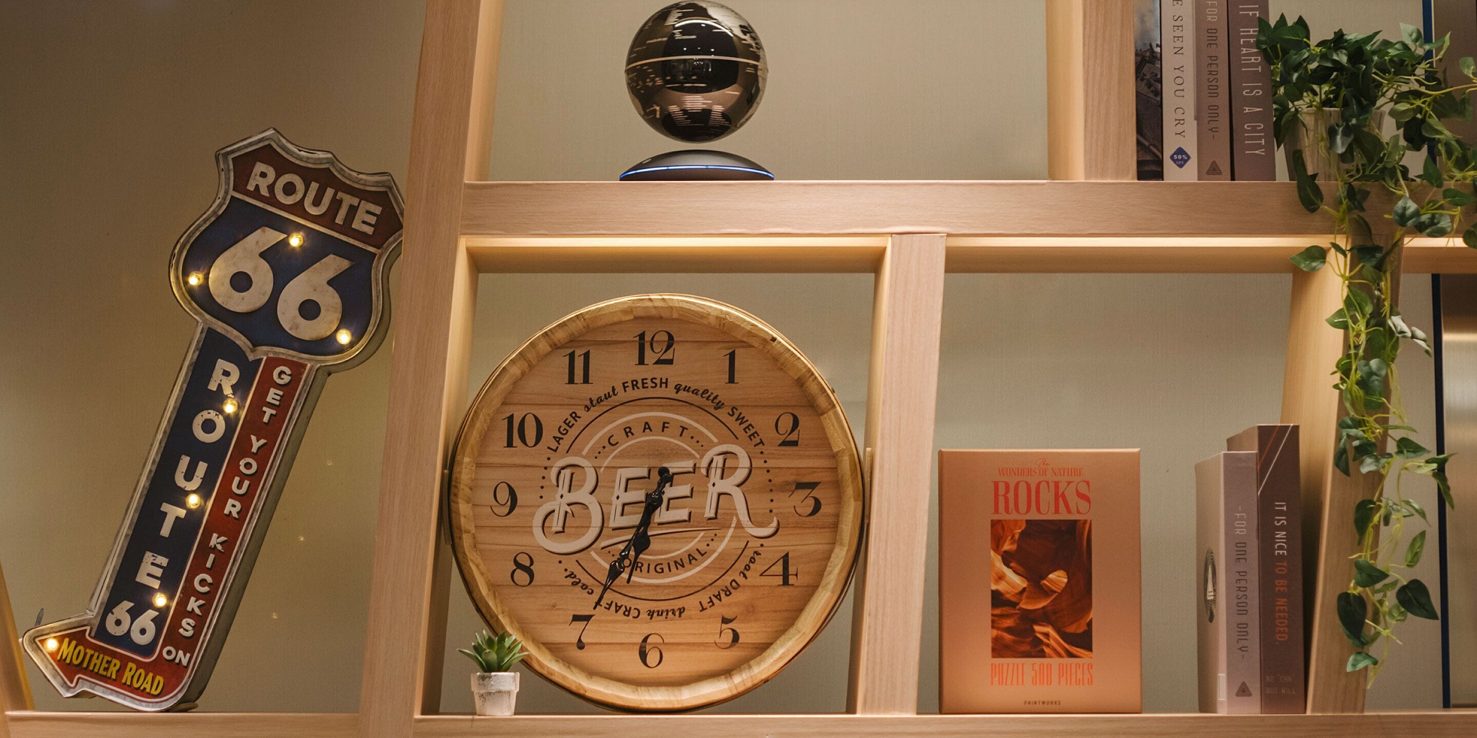 A wooden shelf with a Route 66 sign, a wooden beer clock, a book titled 'The Wonders of Nature Rocks', and a small potted plant.