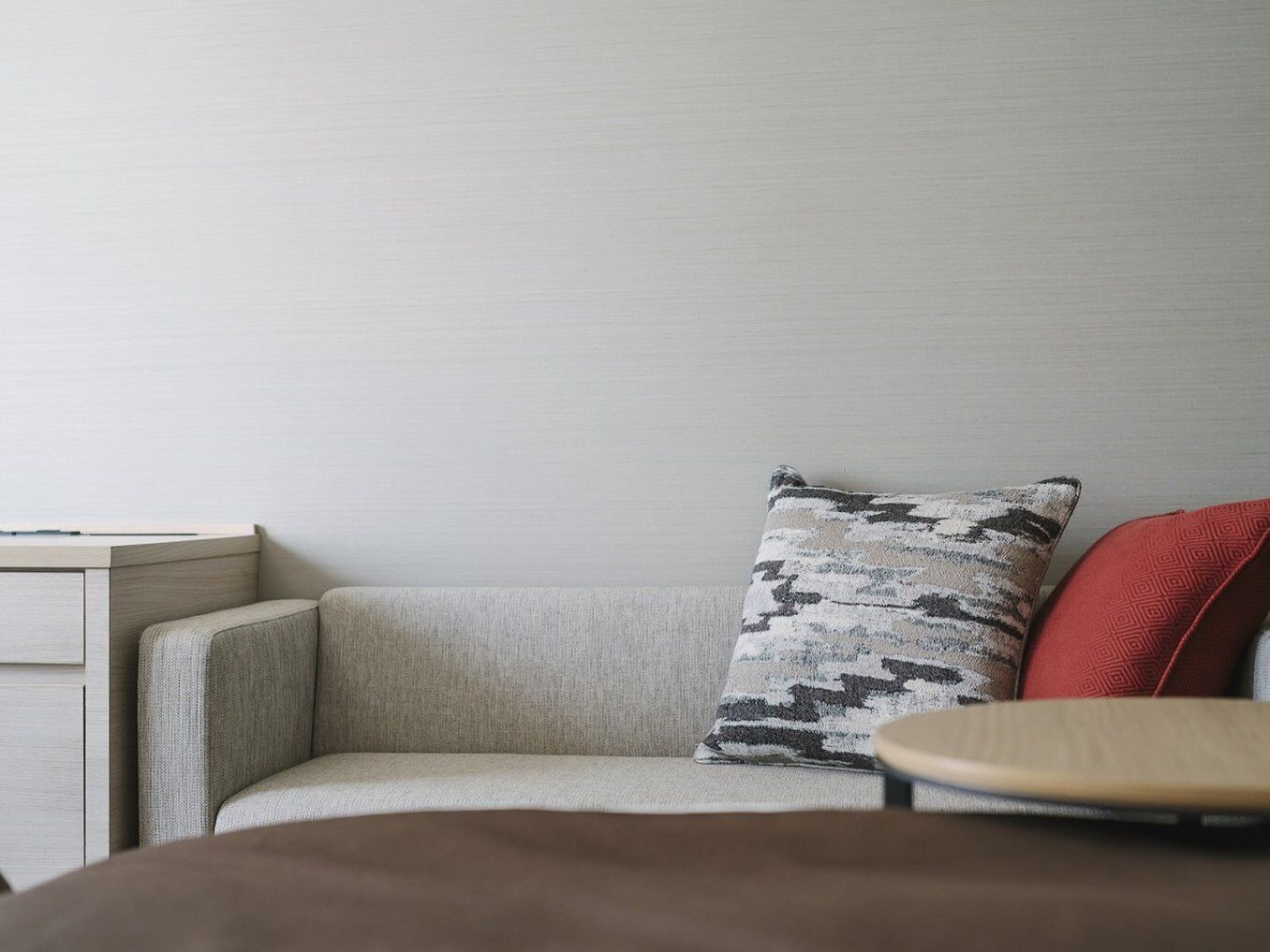 A corner of a room with a light-colored sofa, a patterned pillow, and a red cushion.