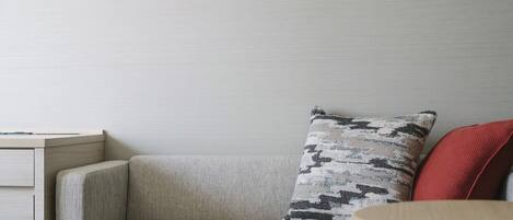 A corner of a room with a light-colored sofa, a patterned pillow, and a red cushion.