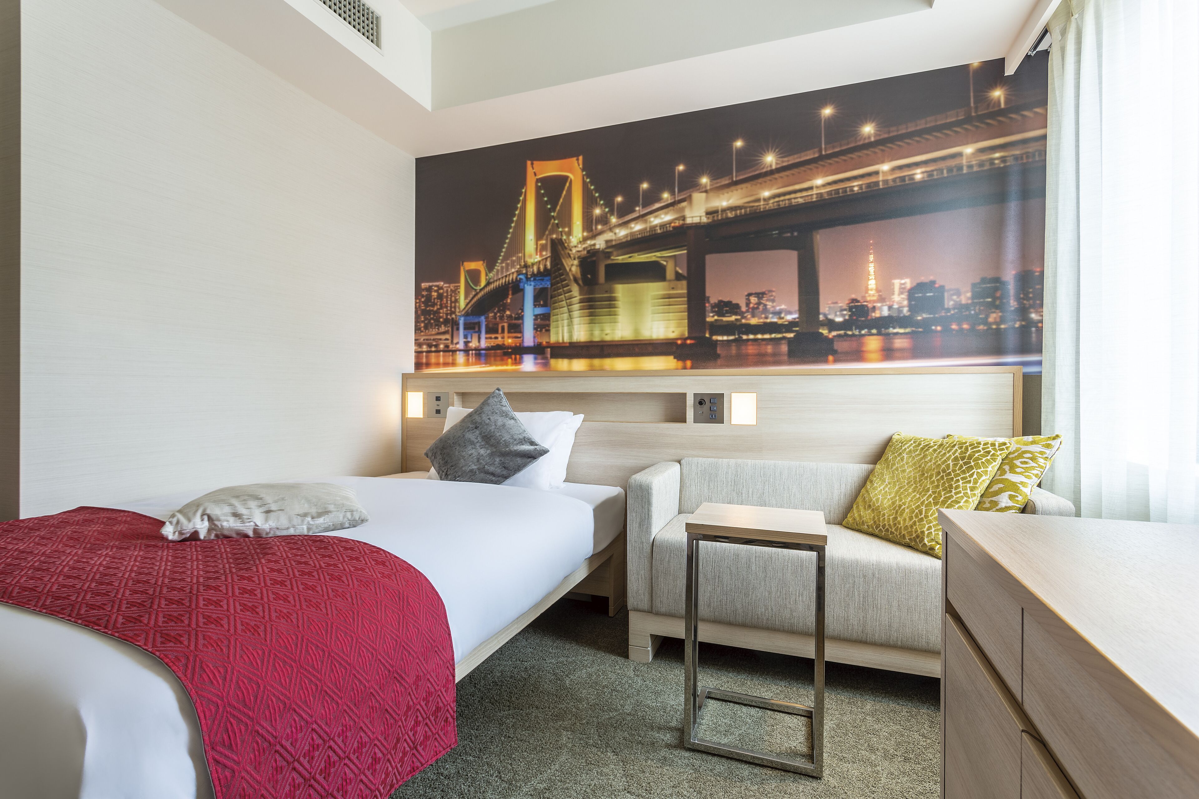 A hotel room with a bed, a sofa, a desk, and a cityscape mural on the wall.
