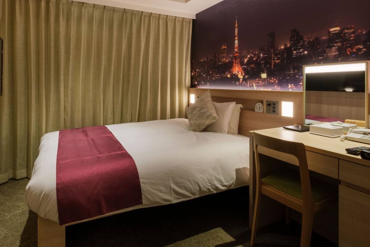 Ein Hotelzimmer mit Bett, Schreibtisch mit Stuhl, Flachbildfernseher an der Wand und Blick auf die Stadt.