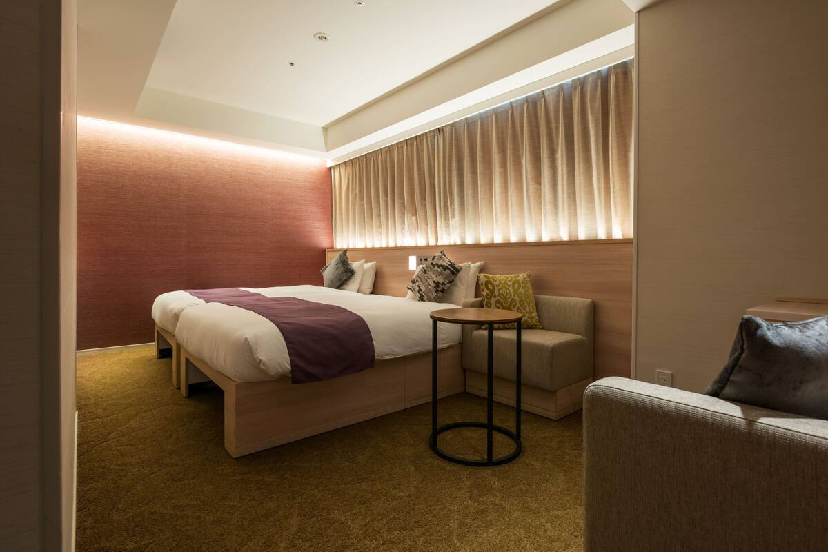 Ein modernes Hotelzimmer mit einem großen Bett, einem kleinen runden Tisch, einer Couch und einem Fenster mit Vorhängen.