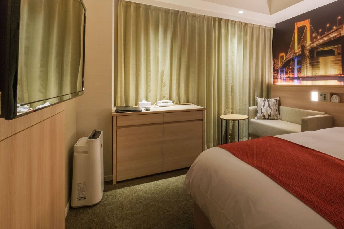 Ein Hotelzimmer mit Bett, Schreibtisch, Stuhl, kleinem Tisch und einem an der Wand montierten Fernseher.