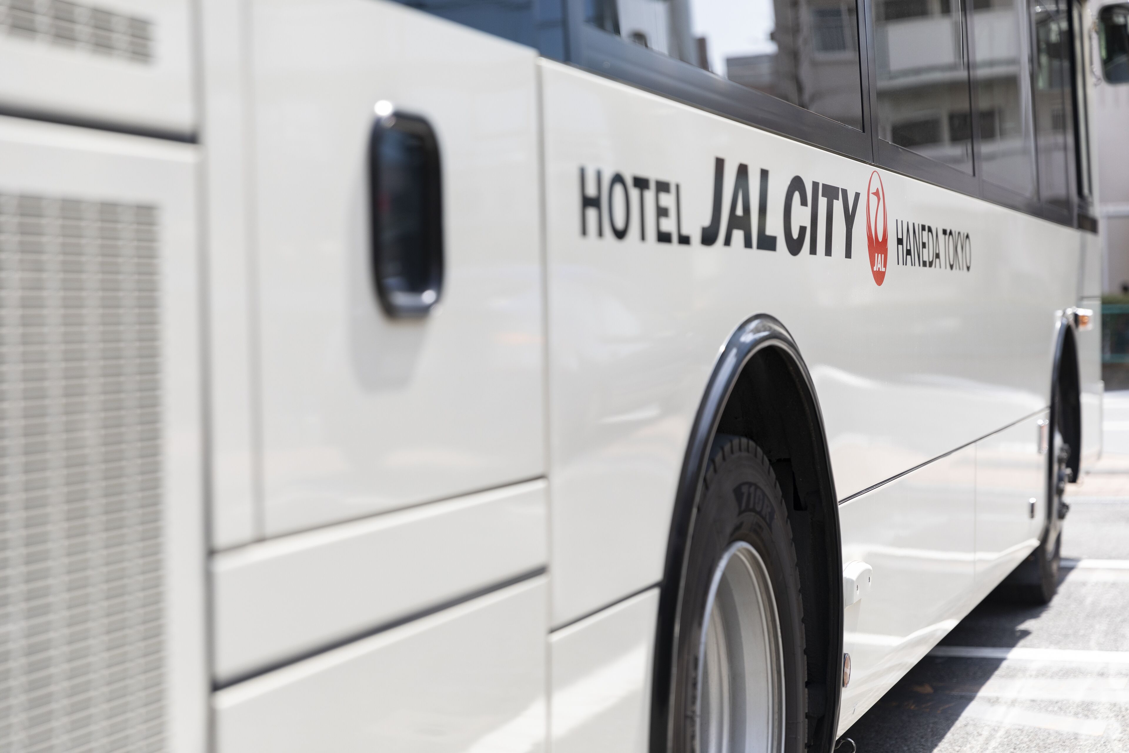 Un autobús blanco con la leyenda 'HOTEL JALCITY HANEDA TOKYO' escrita en la carrocería.