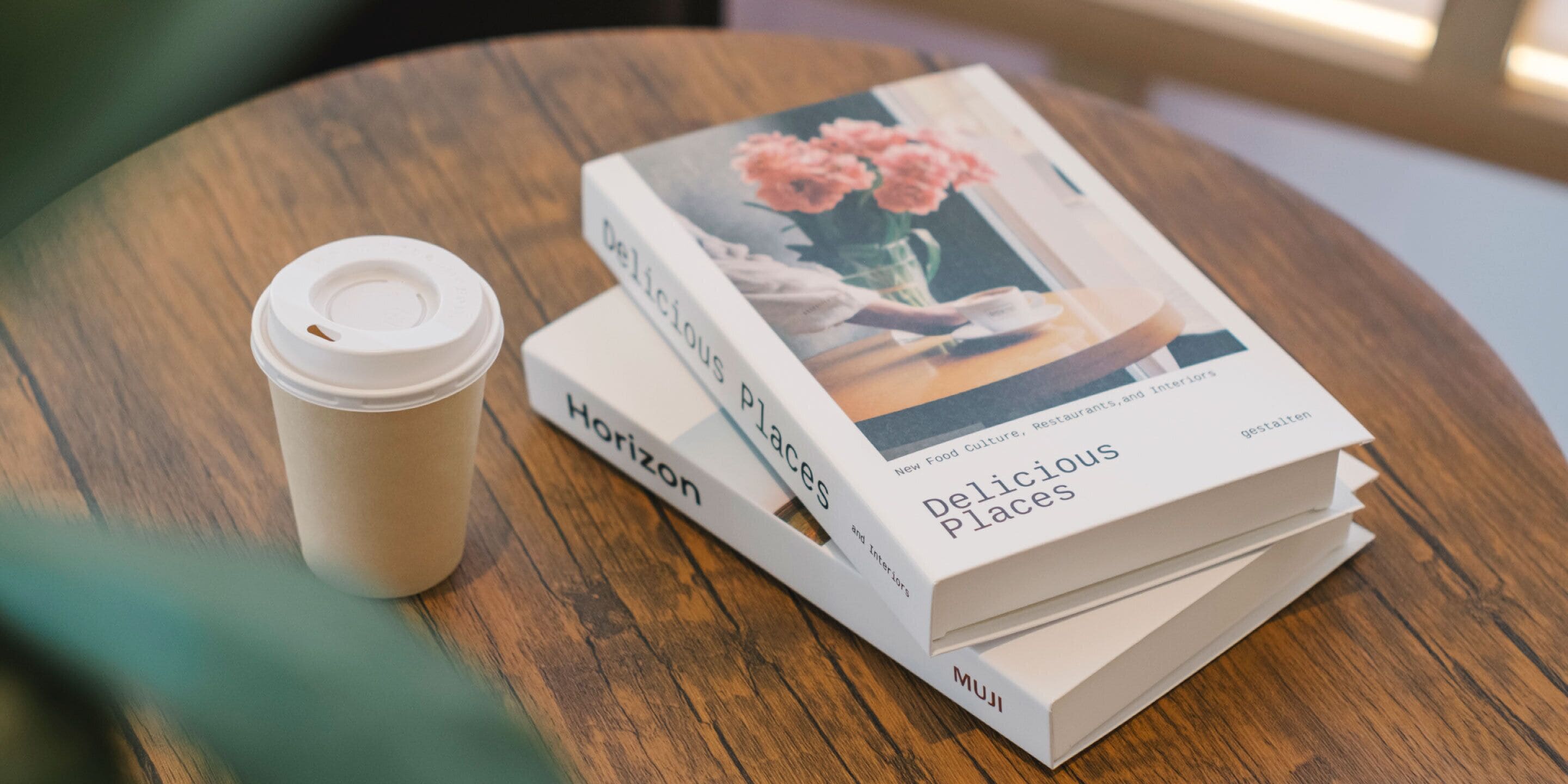 A stack of books titled 'Delicious Places' and a coffee cup on a wooden table.