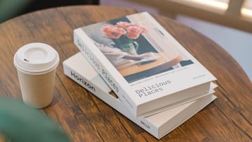 A stack of books titled 'Delicious Places' and a coffee cup on a wooden table.