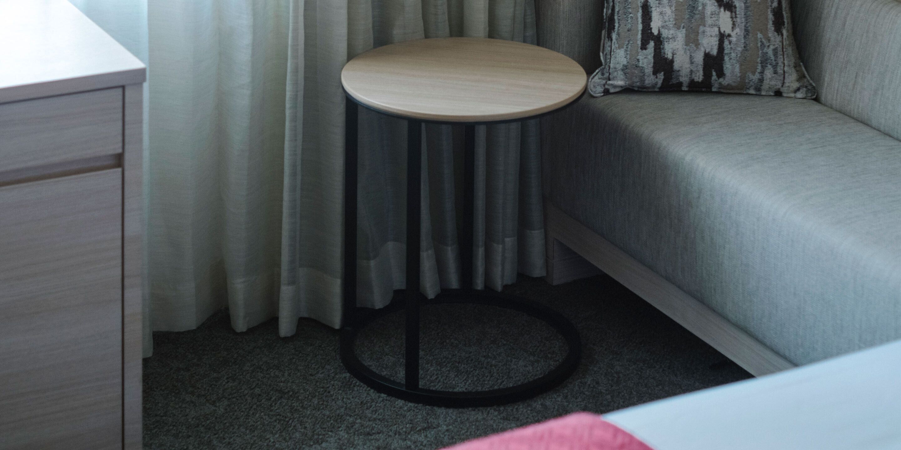A small round table with a wooden top and black base, positioned in a corner of a room with a grey sofa and a white cabinet.