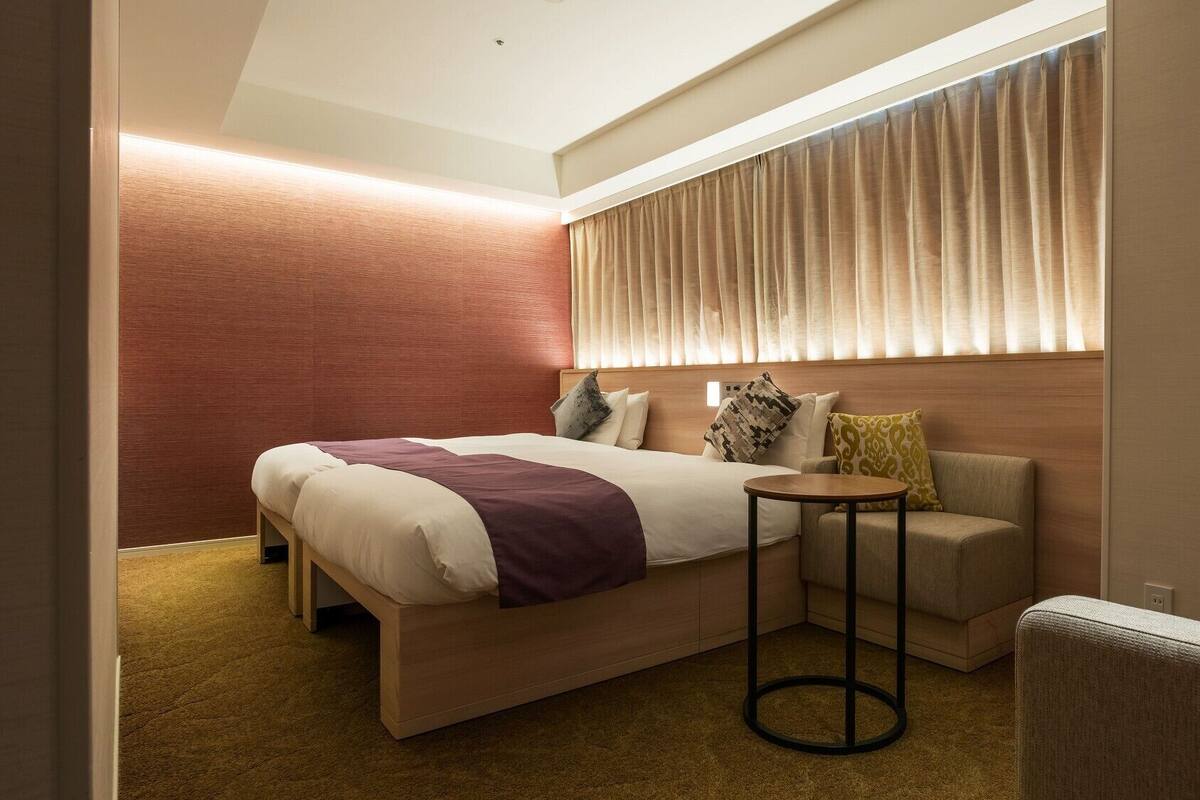 Ein Hotelzimmer mit einem Bett, einem kleinen runden Tisch, einer Couch und einem Fenster mit Vorhängen.