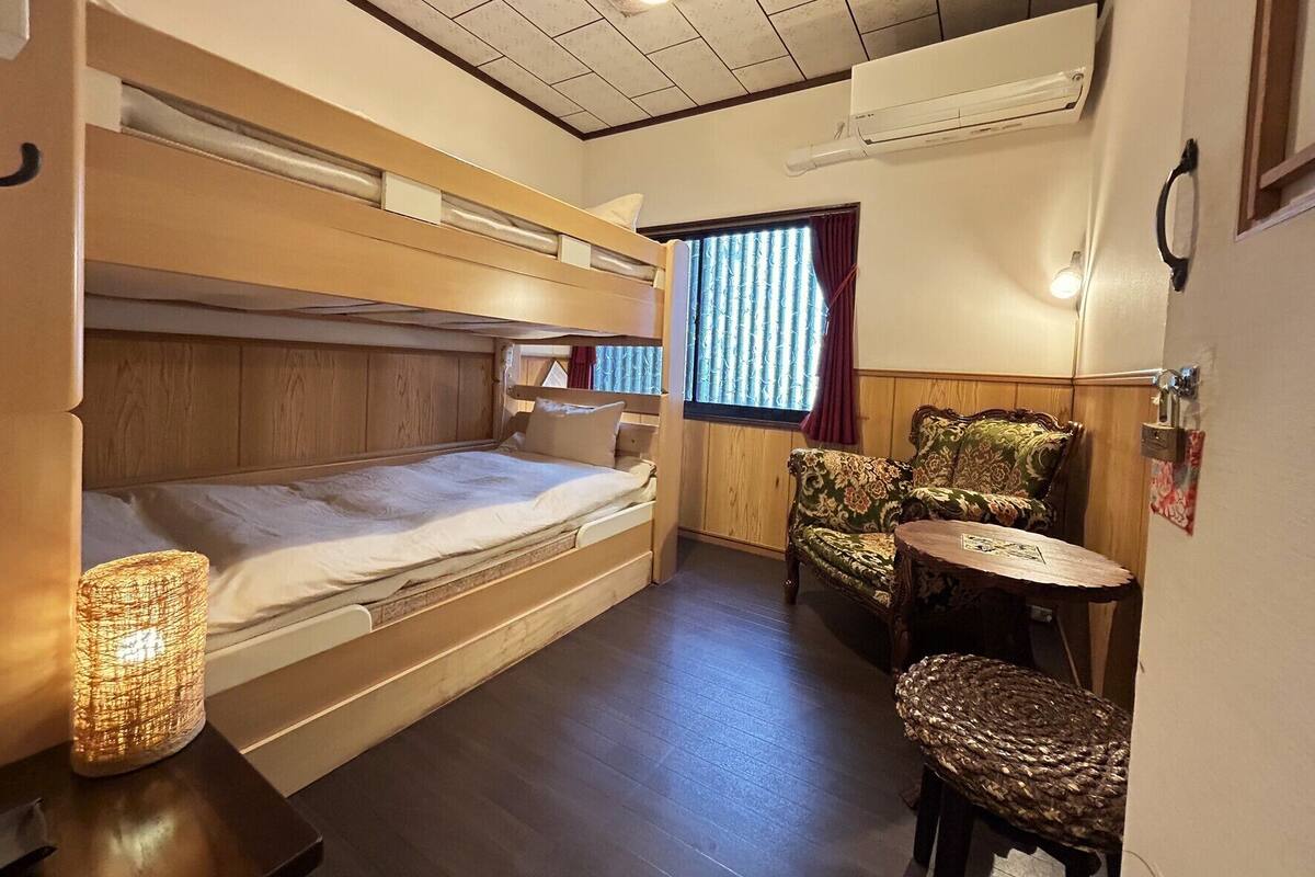 Habitación pequeña con una cama litera, una mesita redonda, una silla y una ventana con cortinas.
