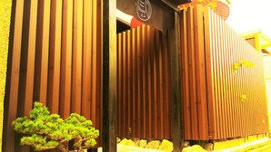 Un edificio con listones de madera verticales, un pequeño bonsái y un letrero que dice 'Guest House Oumi'.