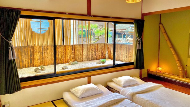 Una habitación con dos camas, un ventanal con vistas a bambú, y una lámpara colgante.