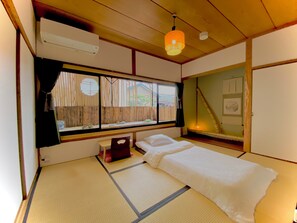 A traditional Japanese room with tatami flooring, a futon bed, a window with shoji screens, and a hanging lamp.