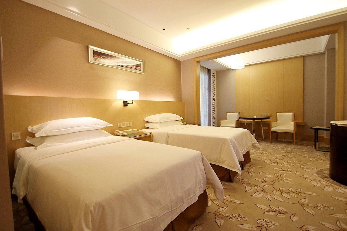 A hotel room with two beds, a desk, a chair, and a small table.