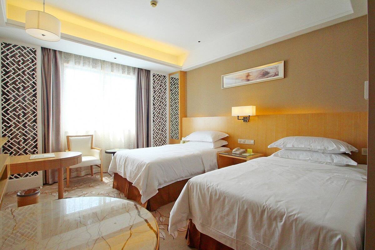 A hotel room with two beds, a desk, and a chair.