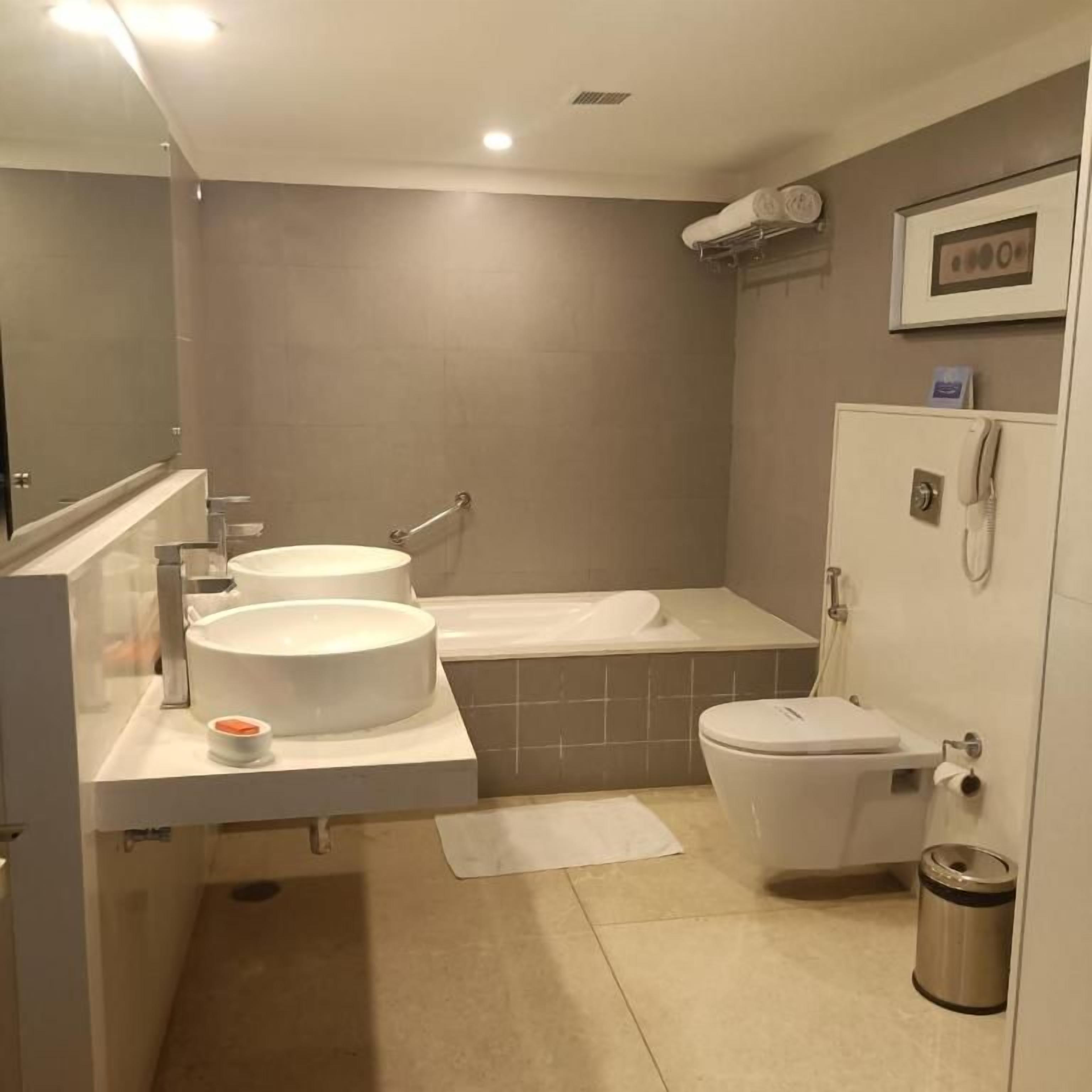 Un baño moderno con una bañera, dos lavamanos, un inodoro y un cubo de basura.