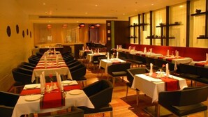 A restaurant with long tables set for dining, chairs, and a bar area. - Royal Park (Kakinada)